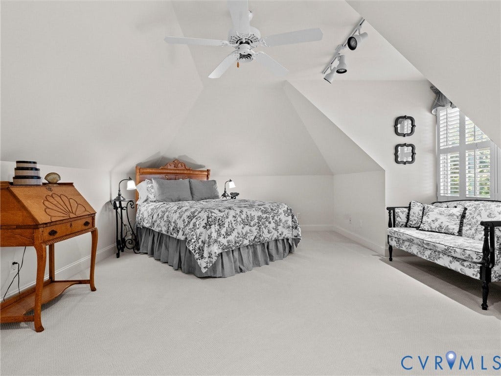 Vaulted ceiling with a ceiling fan, white window shutters, track lighting, and light-toned carpeting