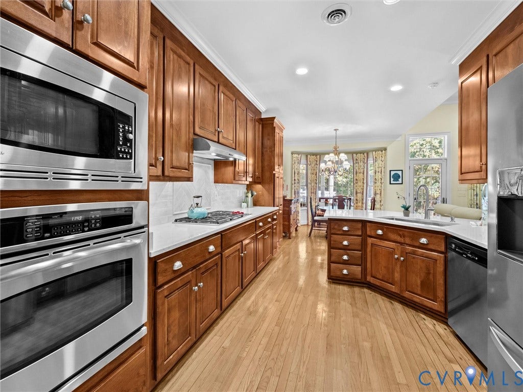 Wood-finish flooring, stainless steel appliances, wood cabinetry, white countertops, and recessed lighting