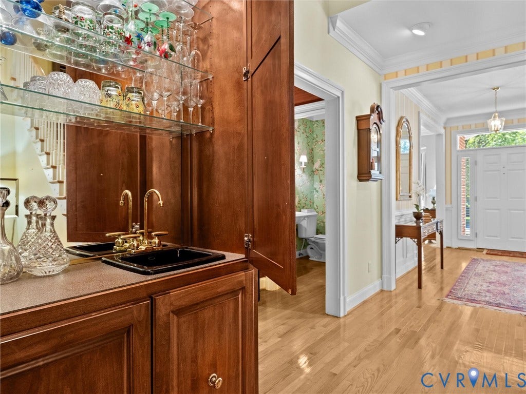 Wet bar featuring wood-finish cabinetry, a mirrored backsplash, and a dual-basin sink with brass-tone fixtures