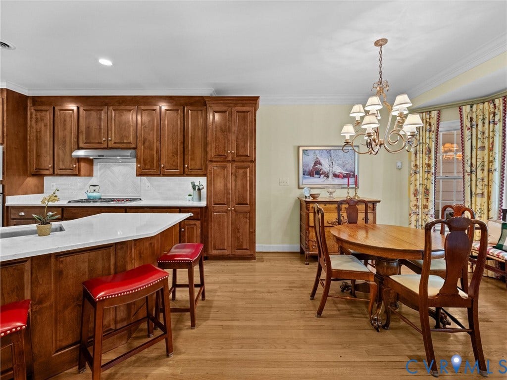 Hardwood flooring, custom wood cabinetry, white countertops, built-in range, and a decorative chandelier