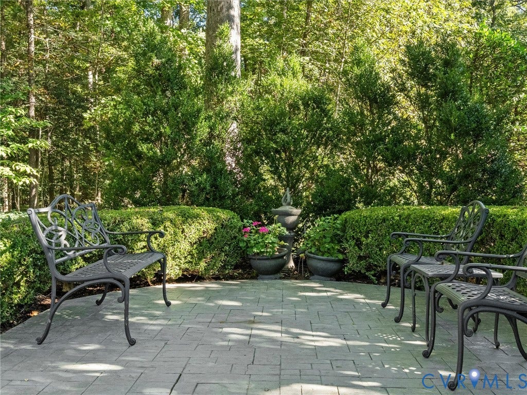 Paved patio with decorative border, surrounded by manicured hedges and mature trees