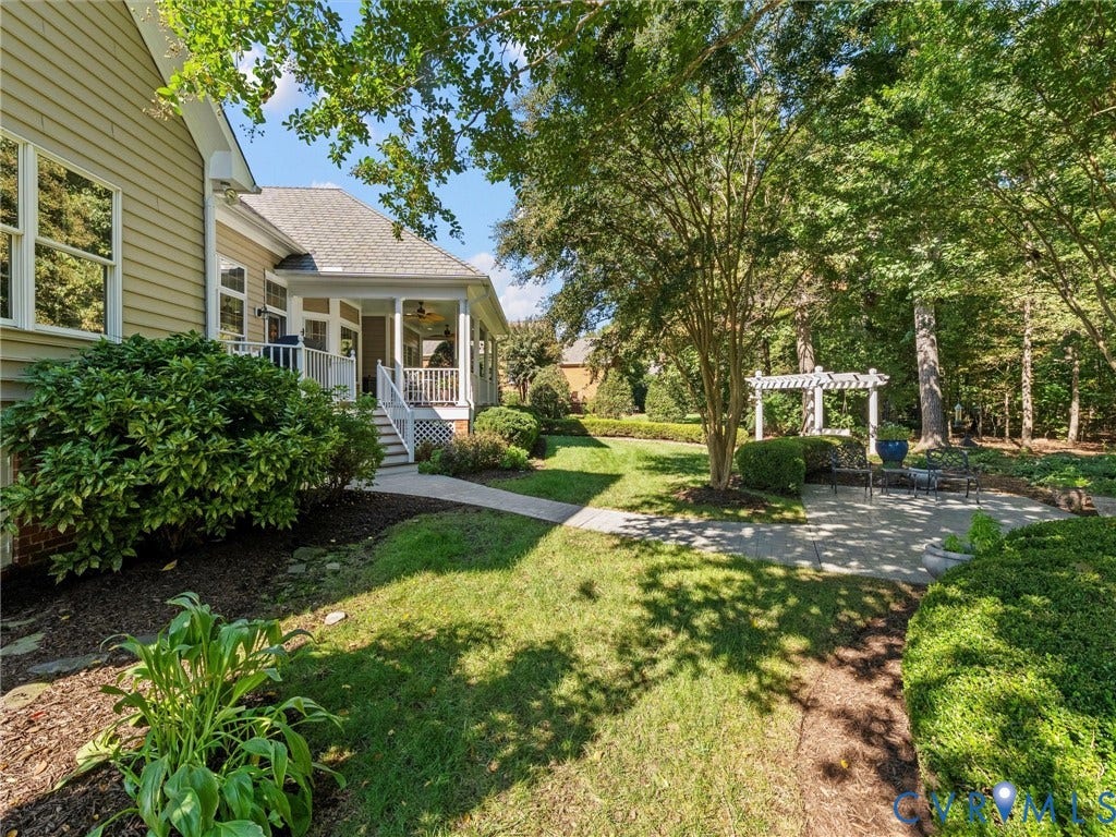 Expansive backyard featuring a manicured lawn, established landscaping, and a covered porch with white railings