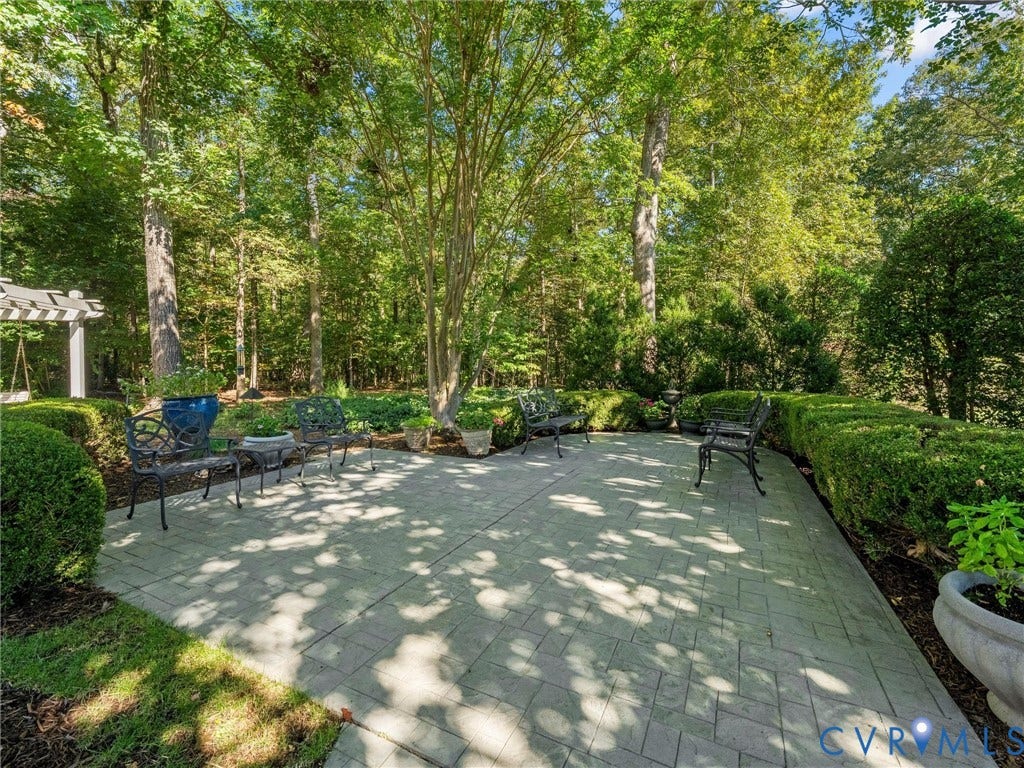 Paver patio with a pergola, surrounded by mature trees and manicured hedges