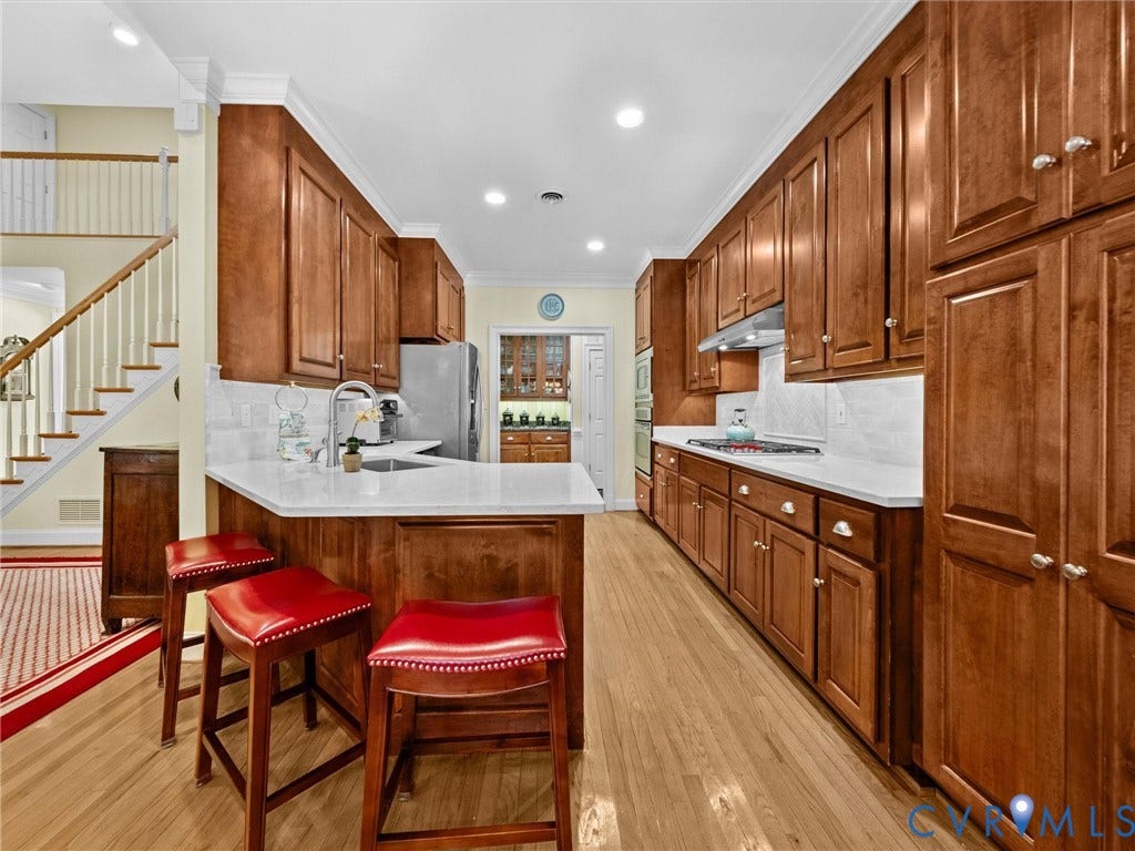 Galley kitchen featuring wood cabinetry, stainless steel appliances, light-toned countertops, and wood-finish flooring