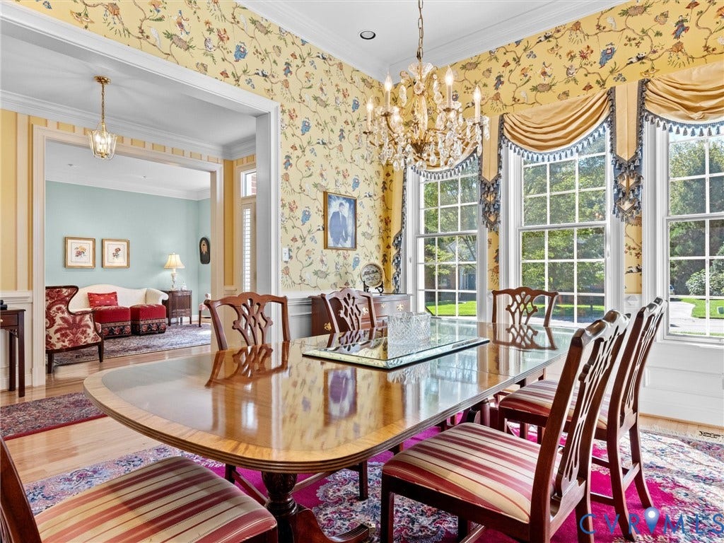 Dining area featuring a crystal chandelier, intricate patterned wallpaper, large bay windows with custom valances, and wood-finish flooring