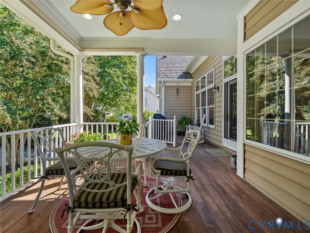 Covered porch featuring wood-finish decking, white railings, and a ceiling fan