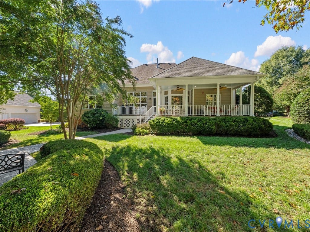 Expansive rear yard with a covered patio, white railing, mature landscaping, and a paver walkway