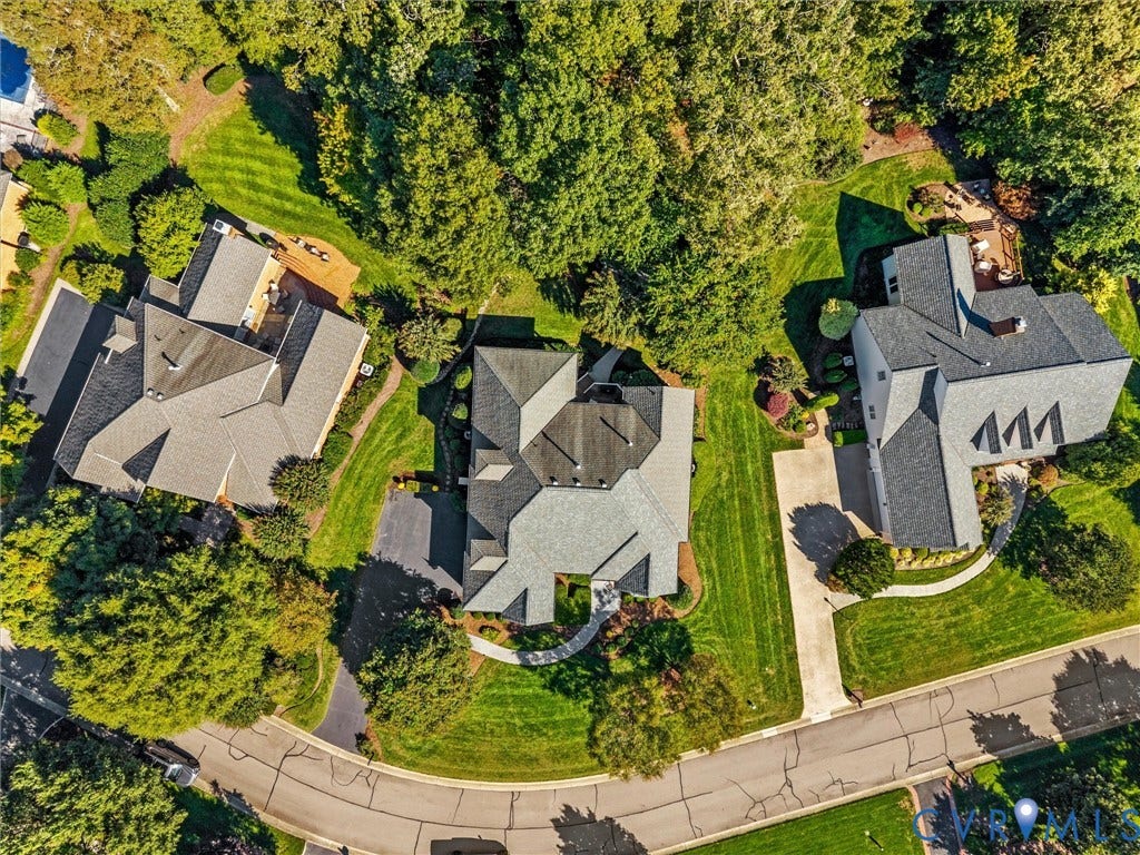 Gable rooflines with multiple dormers, extensive tree coverage, and a paved driveway