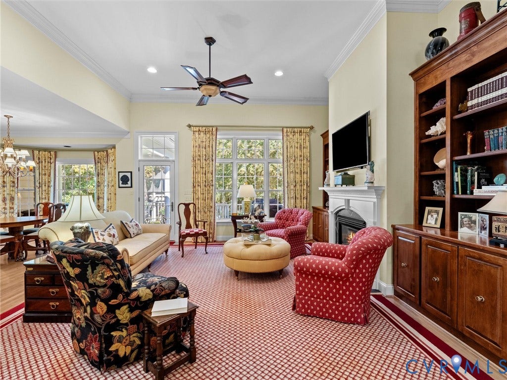 Spacious living area featuring a fireplace with a white mantel, built-in wooden shelving, and a ceiling fan