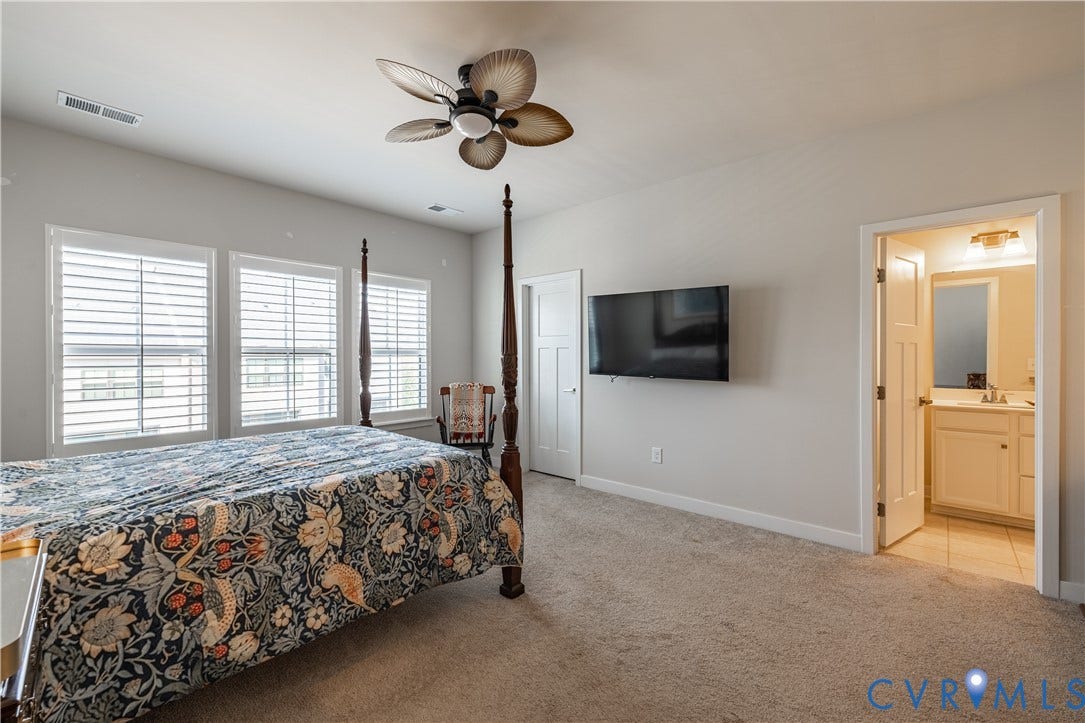14336 Altavista Boulevard, Midlothian, VA 23114 Carpeted room featuring a ceiling fan, three windows with blinds, a wall-mounted television, and a doorway opening to a bathroom with a vanity and mirror