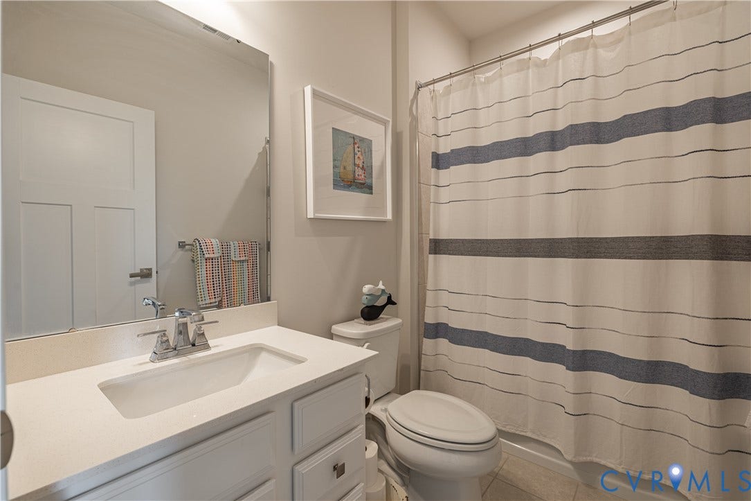 14336 Altavista Boulevard, Midlothian, VA 23114 White vanity with an integrated sink and chrome faucet, large frameless mirror, and a toilet with an adjacent shower area