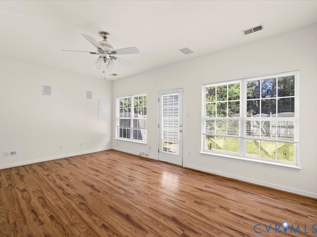 Wood-finish flooring, white walls, ceiling fan with integrated lighting, glass-paned door, and large multi-pane windows