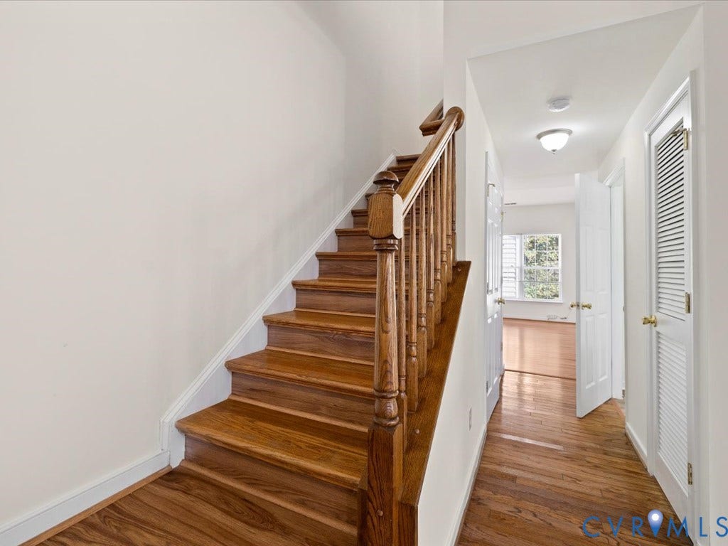 Hardwood flooring, wood staircase with baluster railing, white interior doors, and a ceiling-mounted light fixture