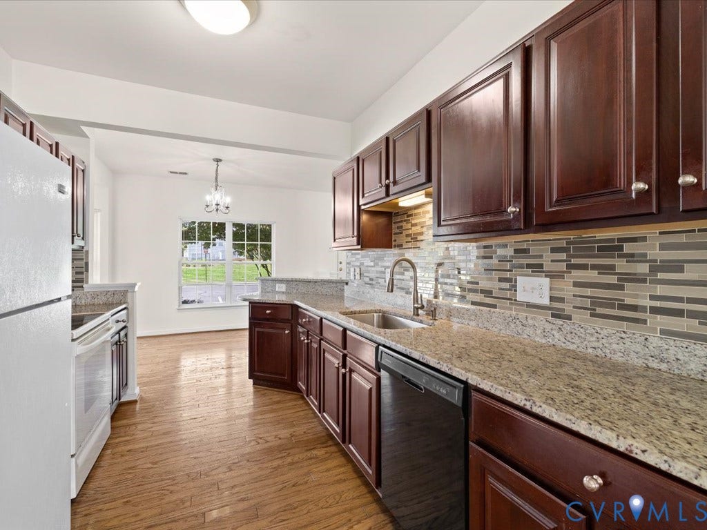 Wood-finish flooring, dark wood cabinetry, granite countertops, tile backsplash, and a stainless steel sink