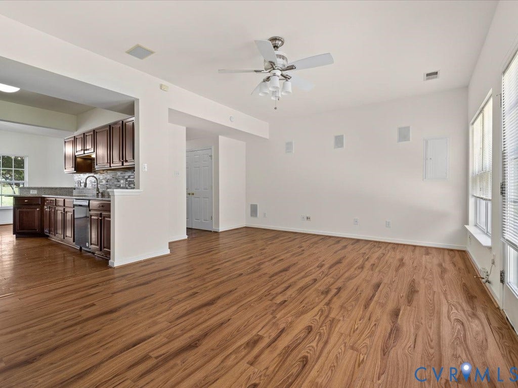 Open-concept living area with wood-finish flooring, a ceiling fan, and multiple windows