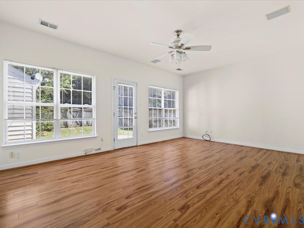 Wood-finish flooring, white walls, multiple windows, a ceiling fan, and a white door with glass panels
