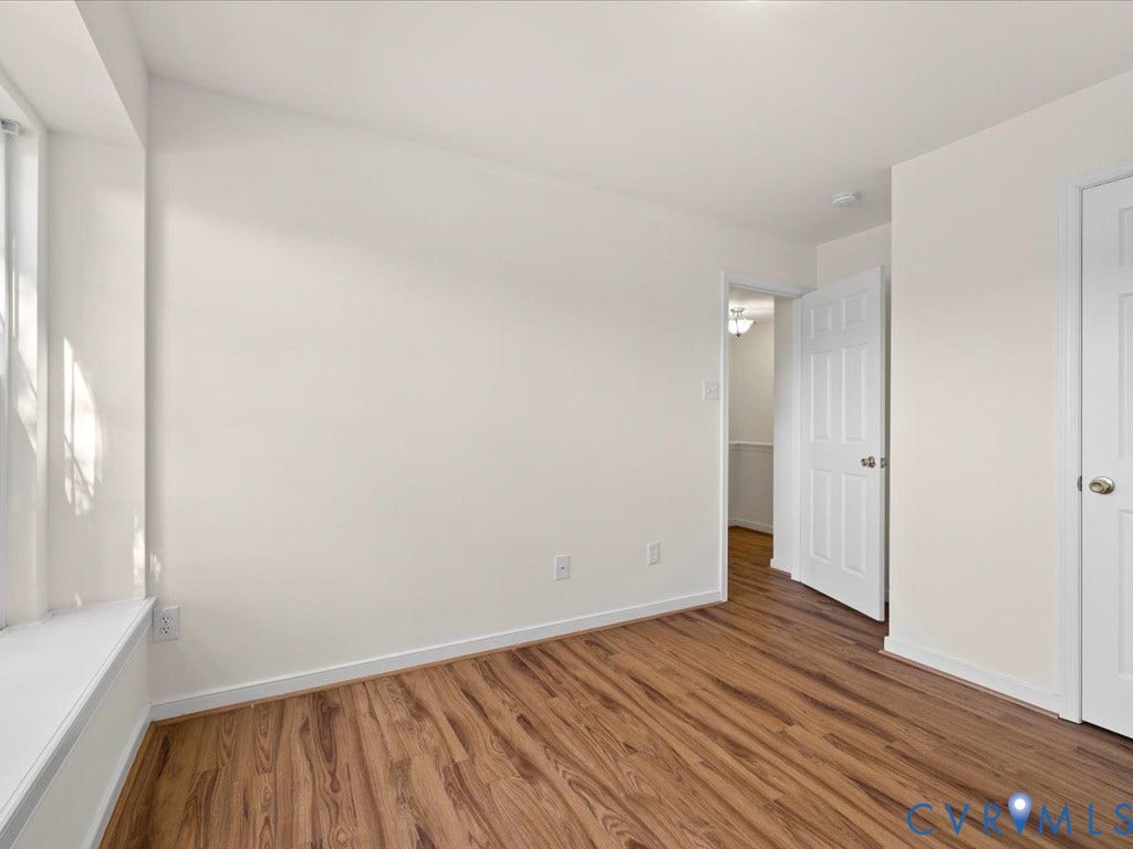 Wood-finish flooring with white baseboards, white walls, and white trim window