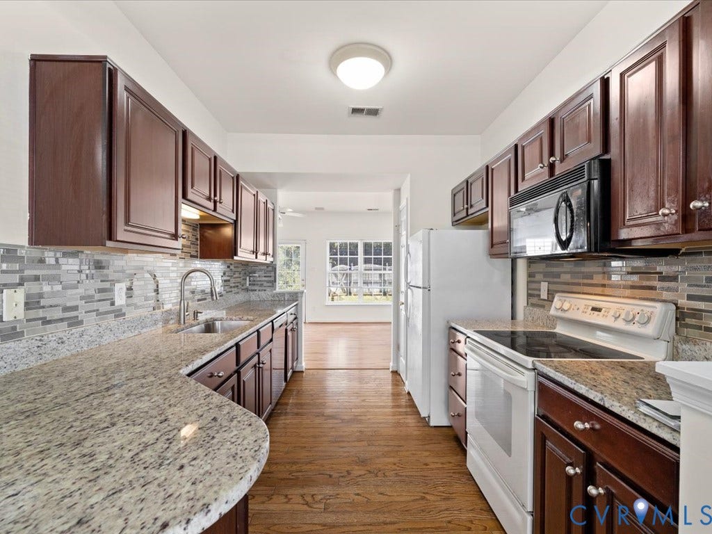 Wood-finish flooring, dark wood cabinetry, light-toned countertops, tile backsplash, and stainless steel sink
