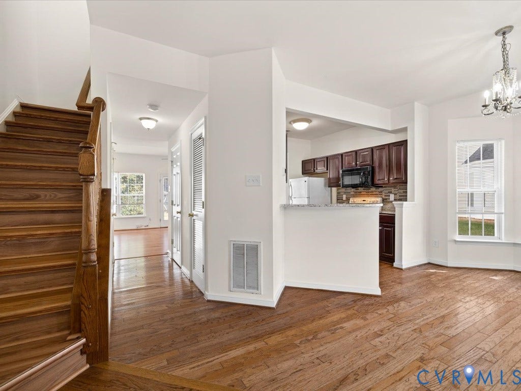 Wood-finish flooring throughout, staircase with wood risers and handrail, kitchen pass-through with breakfast bar, dark wood-finish cabinetry, and a chandelier lighting fixture