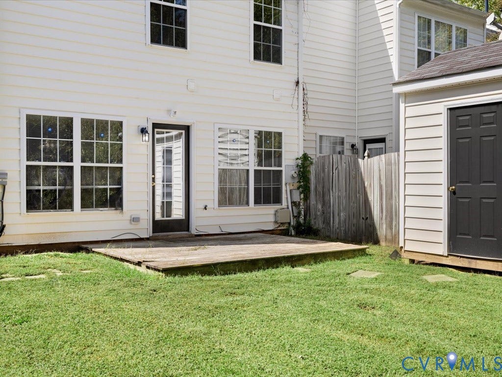 Rear exterior with white siding, ground-level wooden deck, and a detached storage structure featuring a dark paneled door