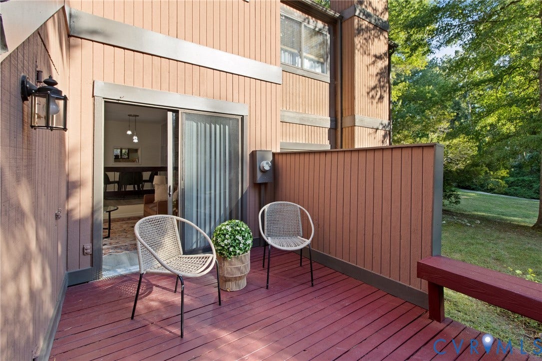 Private outdoor deck with wood flooring, sliding glass door entry, exterior wall lantern, and built-in privacy wall