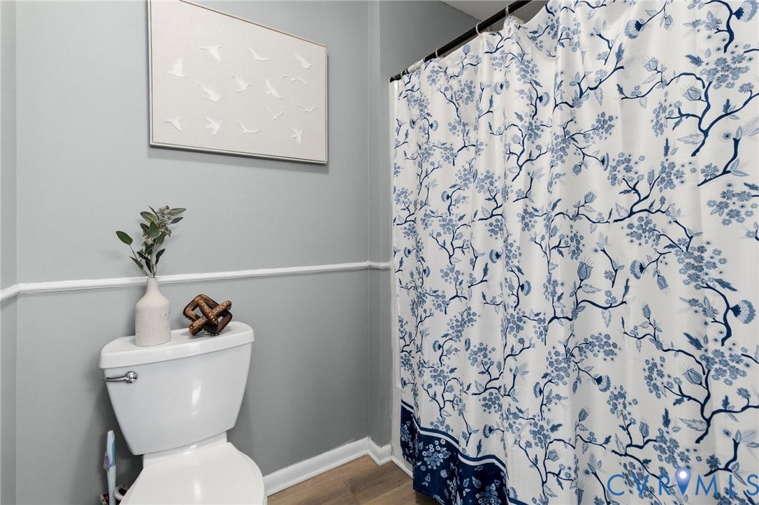 White toilet with chrome flush lever, light grey walls with decorative trim, and wood-finish flooring