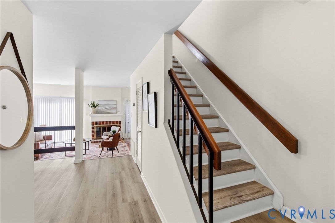 Wood-finish flooring, staircase with wood handrail, fireplace with brick surround, and vertical blinds