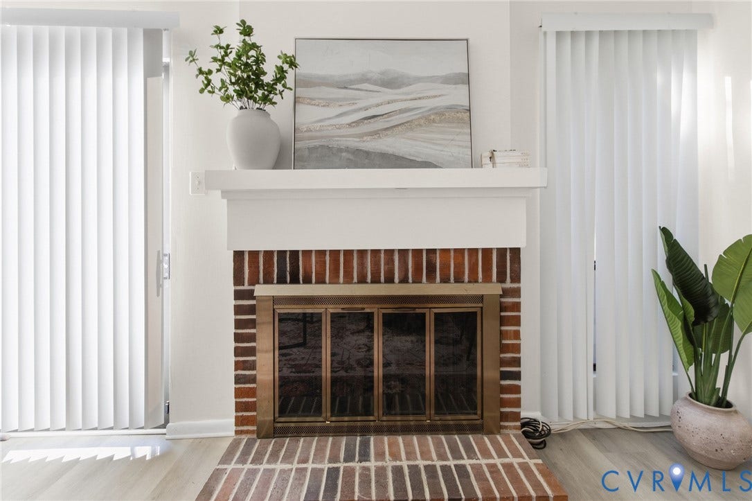 Brick fireplace featuring a brass firebox, white mantel, and light wood-finish flooring
