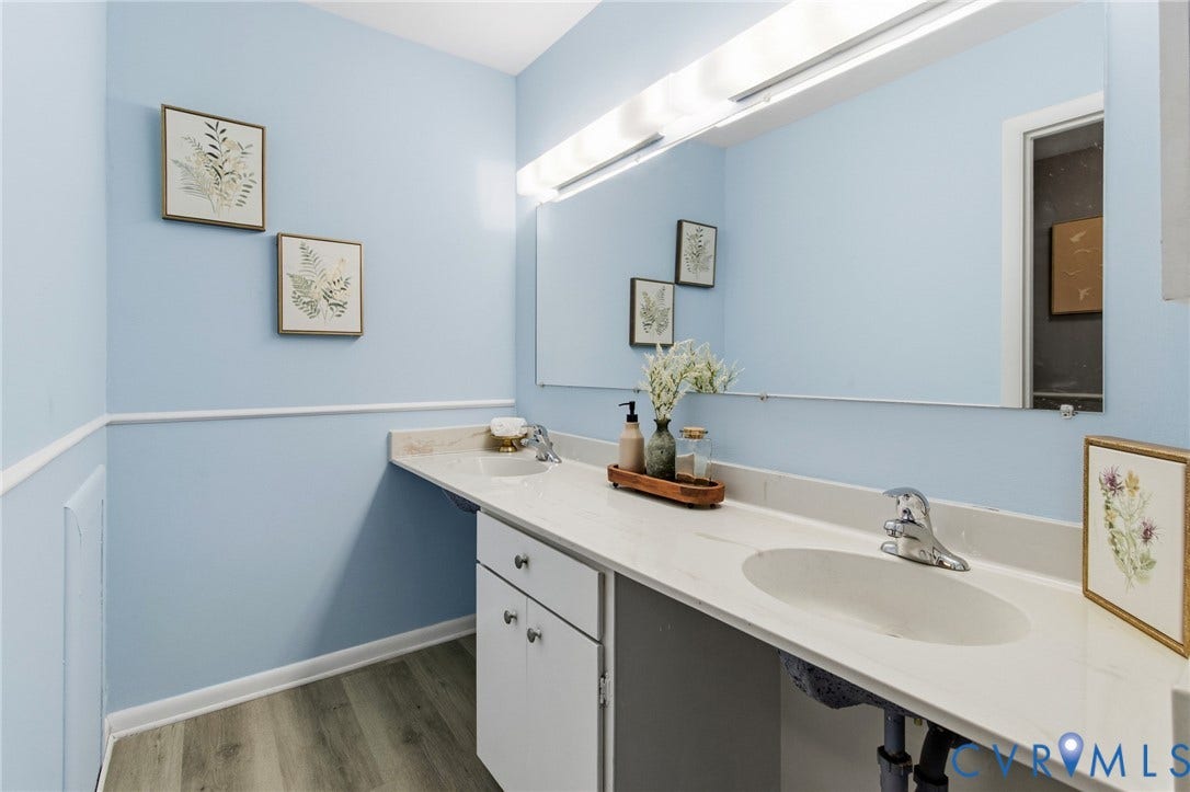Dual vanity with integrated sinks, expansive counter space, wood-finish flooring, and a large wall-mounted mirror with overhead lighting
