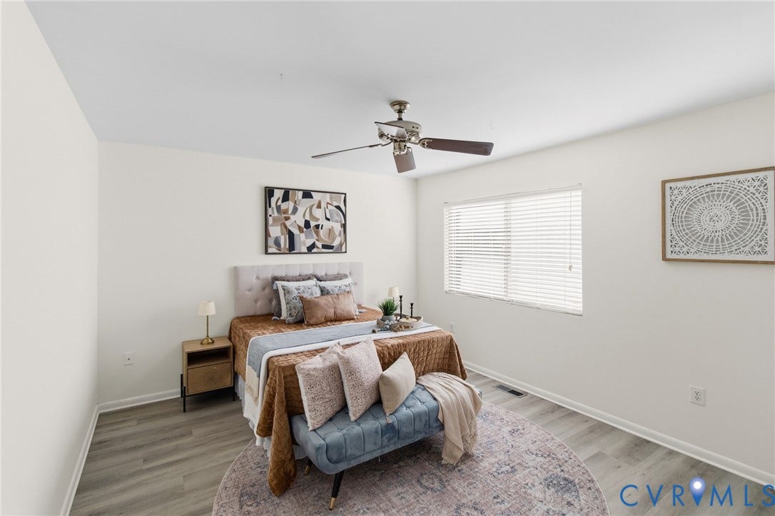 Neutral tone walls, wood-finish flooring, ceiling fan with light, window with blinds, and a built-in wall outlet