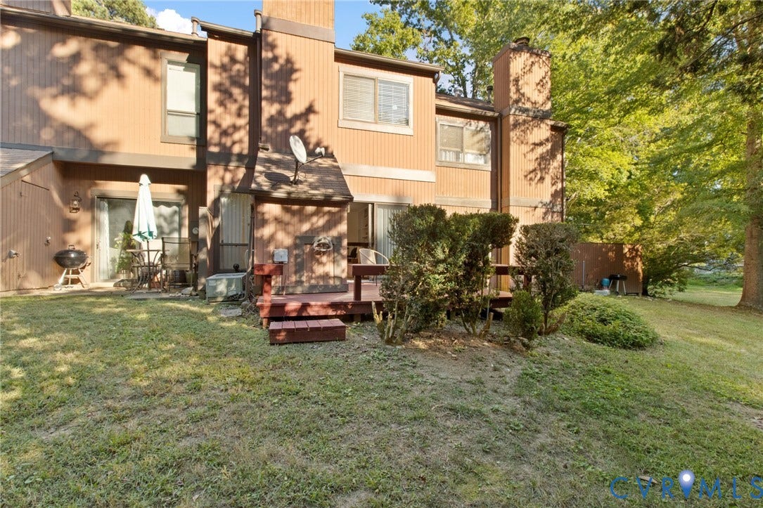 Expansive rear yard featuring a wooden deck with steps, a concrete patio, and mature trees