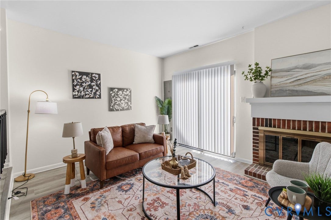 Living area featuring wood-finish flooring, a brick fireplace with a white mantel, and a sliding glass door with vertical blinds