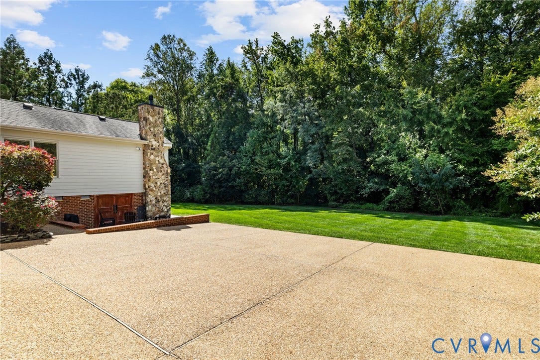 3808 Barrington Branch Court, Henrico, VA 23233 Expansive concrete patio with a full stone chimney, siding exterior, and a manicured lawn framed by mature trees