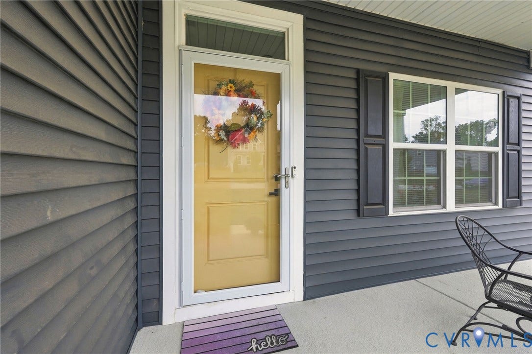 Yellow paneled door with white storm door, dark gray horizontal siding, and white window trim