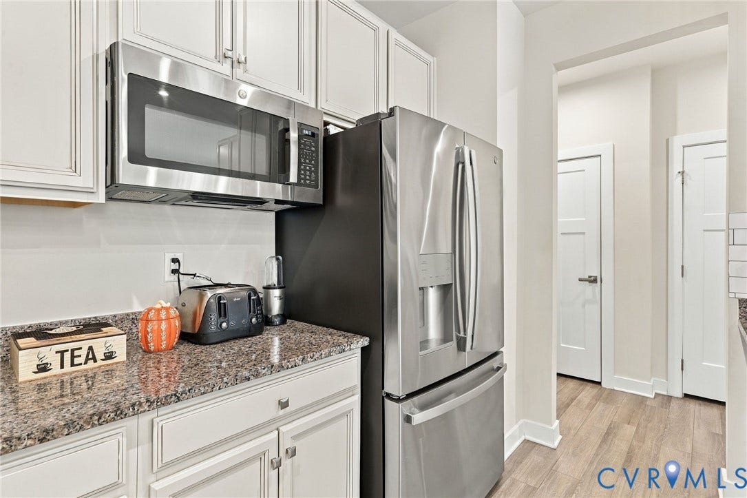 Stainless steel microwave, stainless steel refrigerator, white cabinetry, granite countertops, wood-finish flooring