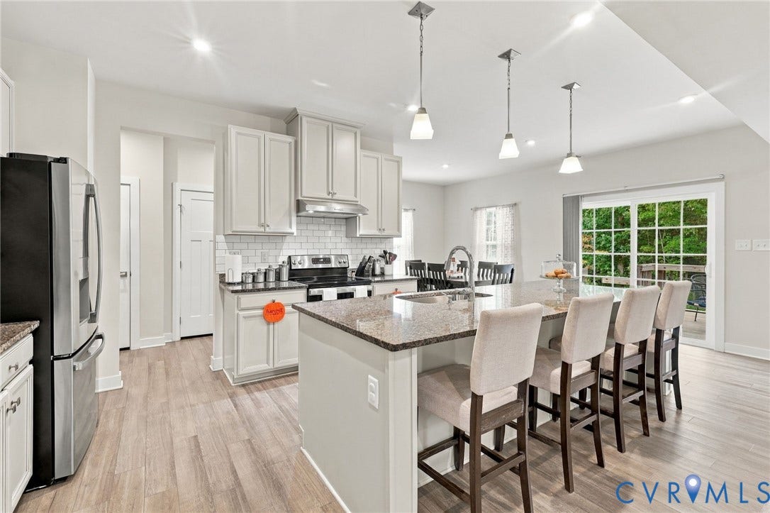 Gourmet kitchen featuring a large island with seating, stainless steel appliances, white cabinetry, a subway tile backsplash, and light wood-finish flooring
