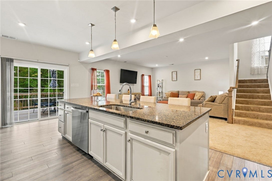 Open-concept living space featuring a central kitchen island with a double basin sink, recessed lighting, wood-finish flooring, and a sliding glass door