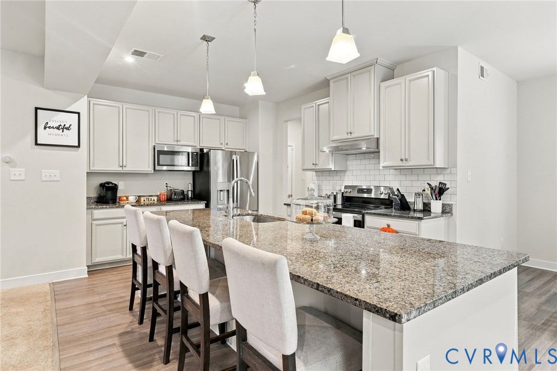 Kitchen featuring an oversized island with a built-in sink, pendant lighting, stainless steel appliances, white shaker cabinetry, and subway tile backsplash