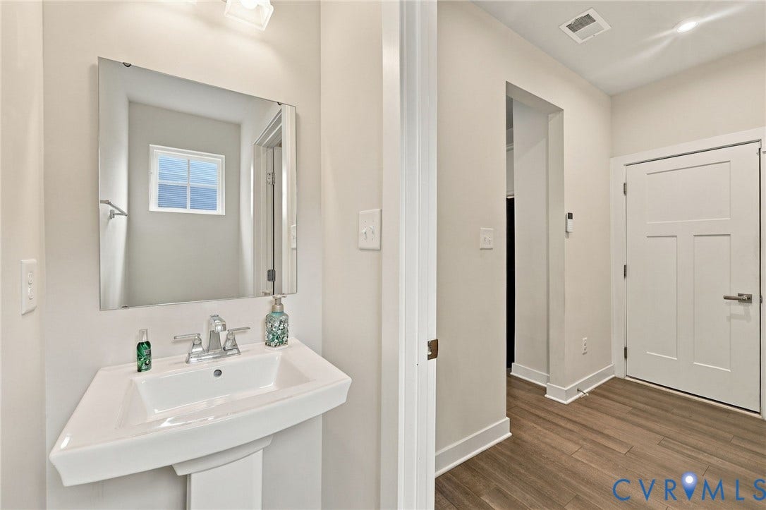 Pedestal sink with chrome faucet, framed mirror, and wood-finish flooring