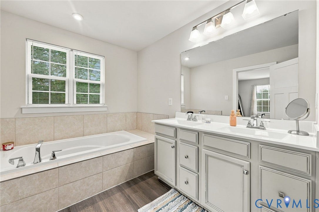 Double vanity with undermount sinks, wood-finish flooring, recessed lighting, and a built-in soaking tub with tiled surround