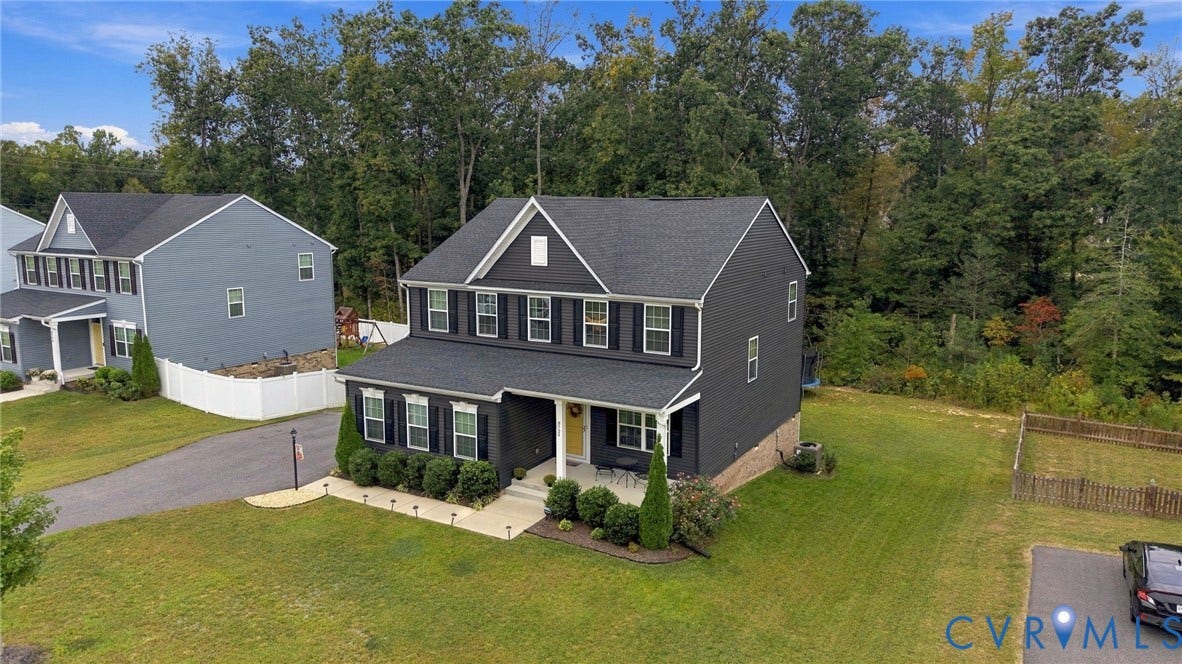 Charcoal gray siding with white trim, black shutters, covered front porch, and mature landscaping