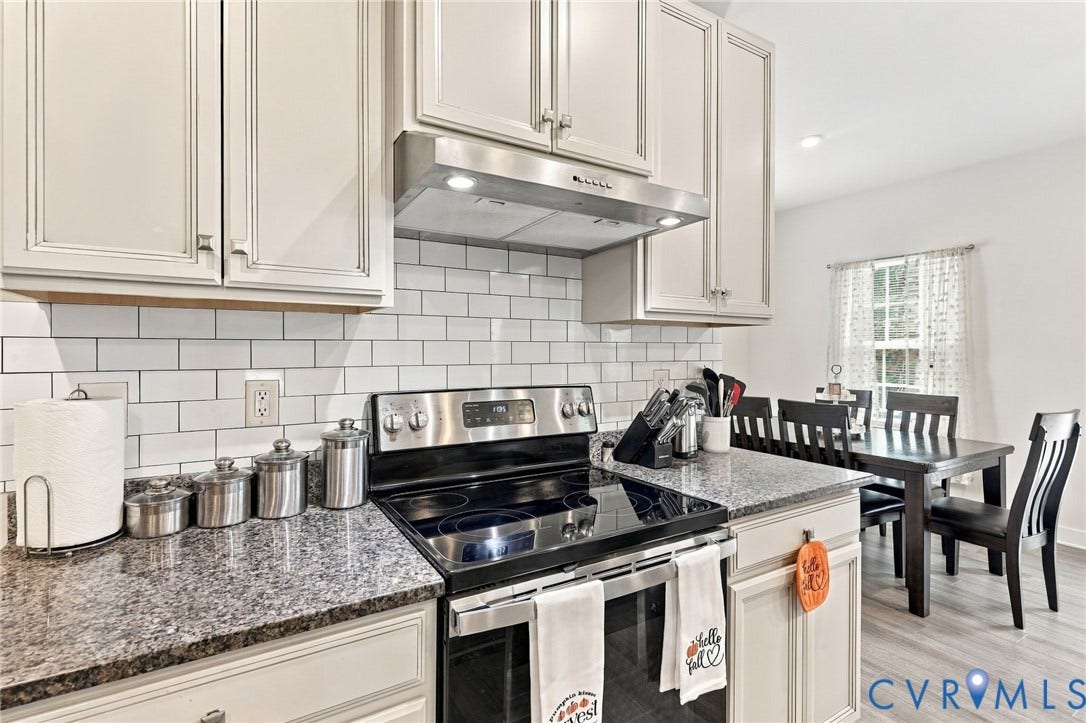 Kitchen featuring light-toned cabinetry, subway tile backsplash, stone-finish countertops, and a stainless steel range with overhead ventilation