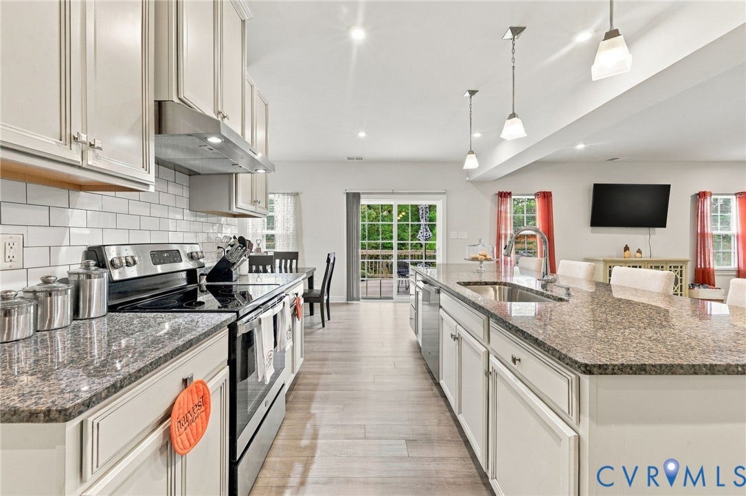 Open-concept kitchen featuring an expansive center island with an undermount sink, granite countertops, and light wood-finish flooring