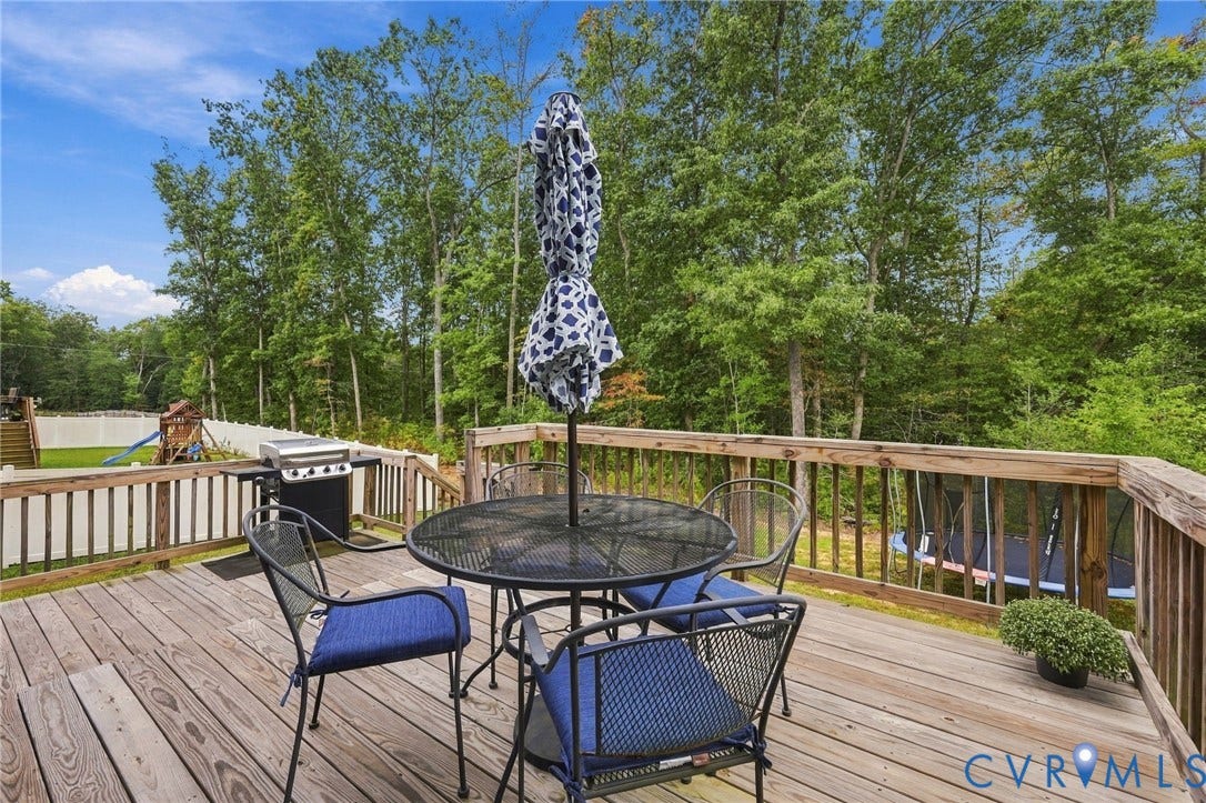 Spacious wood deck with natural wood railings, featuring a built-in grill and surrounding mature trees