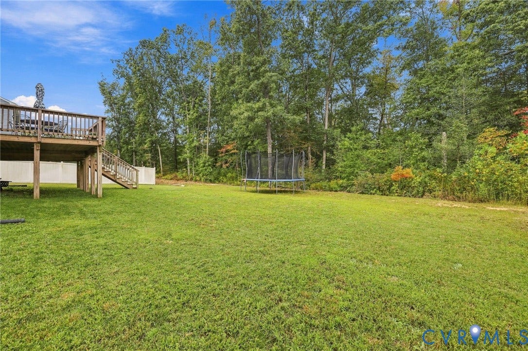 Expansive grassy yard with a wooden deck and staircase