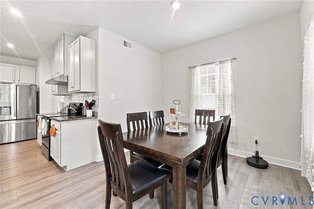 Open-concept living space with wood-finish flooring, white cabinetry, stainless steel appliances, and a window with natural light