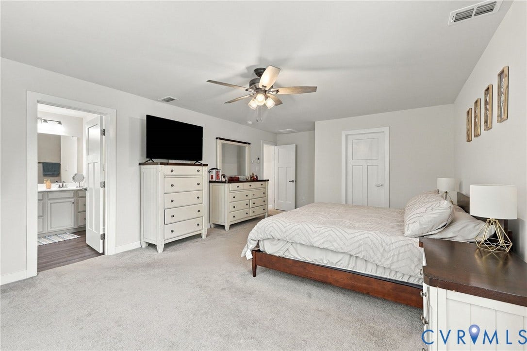 Expansive carpeted room featuring a ceiling fan, white paneled doors, and an en-suite bathroom with a vanity and wood-finish flooring