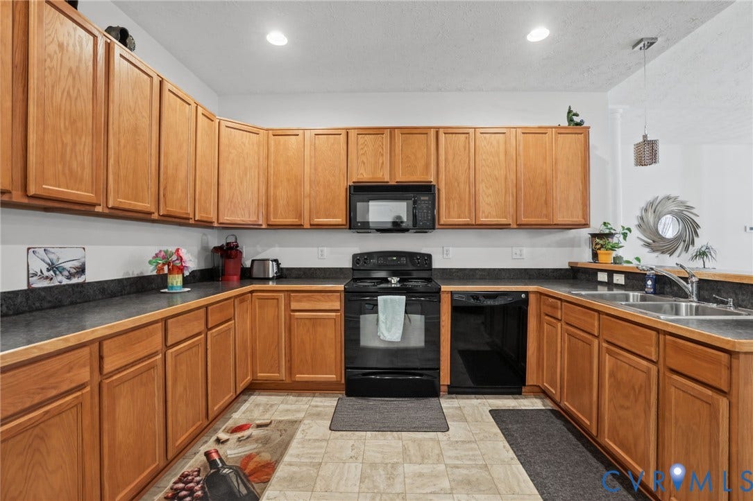 251 Pumpkin Place, Harvest Glen, North Chesterfield, VA 23236 Spacious kitchen featuring warm wood cabinetry throughout, black gas range with matching microwave, dark countertops, recessed lighting, and tile flooring in a U-shaped layout with ample storage and counter workspace