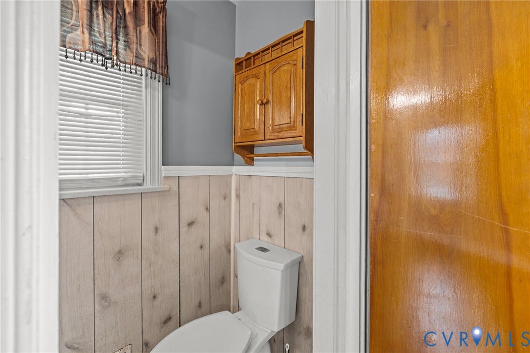 2405 Dumbarton Road, Henrico, VA 23228 White paneled wall with a window, showcasing a toilet and a wooden wall cabinet