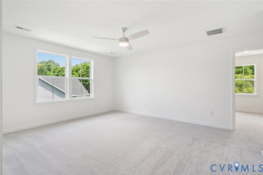 9116 TERROIR Lane, Viniterra Villas, New Kent, VA 23124 Spacious room with light-colored carpeting, multiple windows, and a ceiling fan with integrated lighting